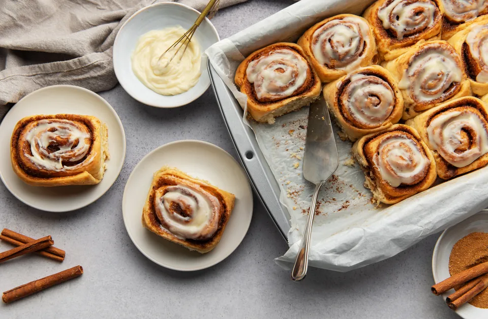 Glazed cinnamon rolls on a baking tray and plates.