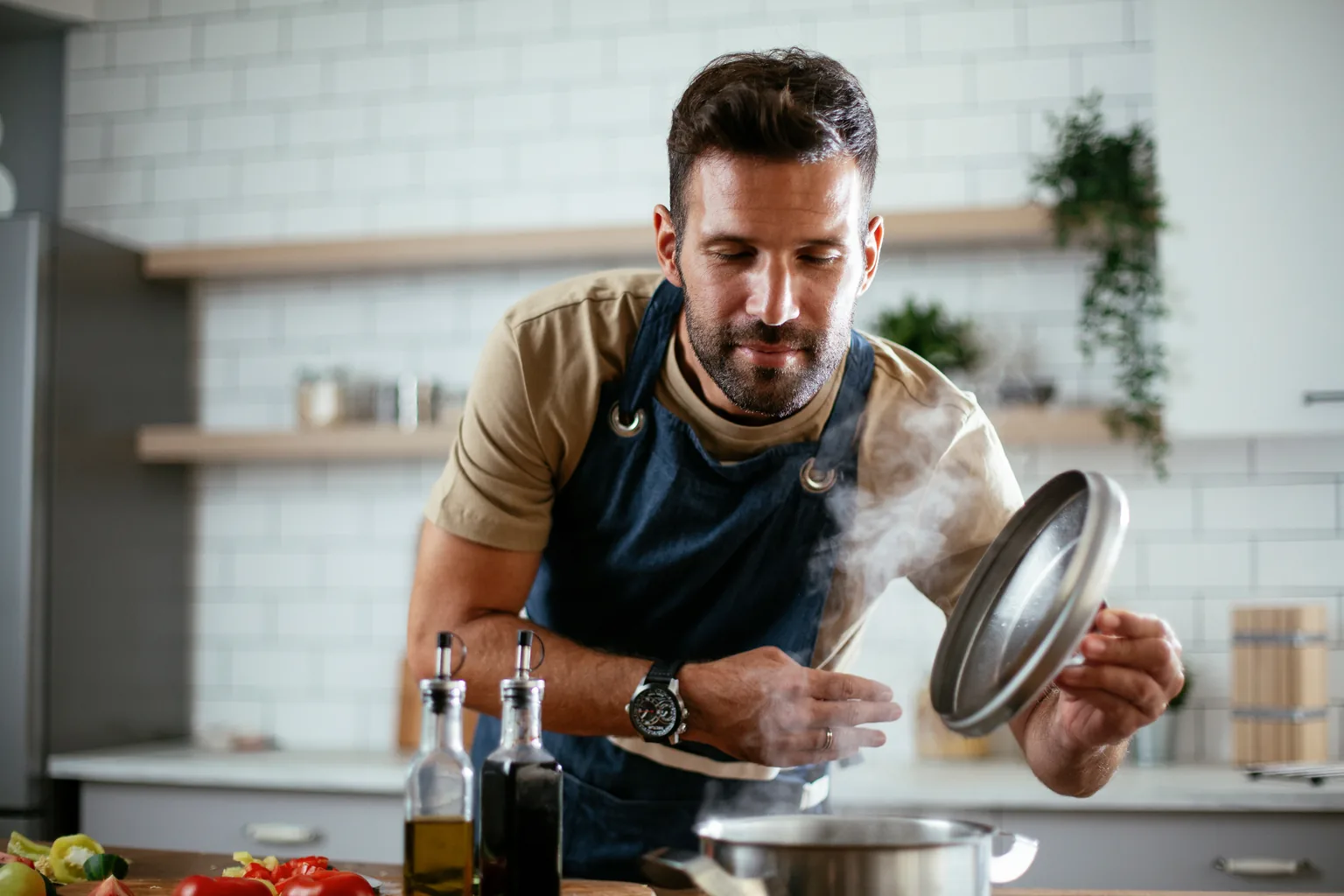 A man lifting the lid of a cooking pot in a home kitchen.